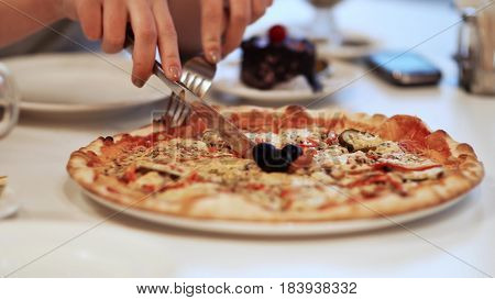 Close-up of a fresh homemade pizza, young girl cuts the pizza
