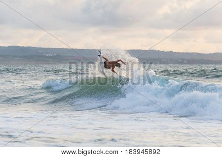 Surfer with a tanned body performs a trick on a short board - a jump over the waves. Extreme water sports, fun at the oceanfront surfing. The surfer rolls on the waves at sunset.