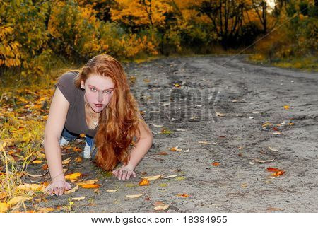 Indoeuropea ragazza con capelli lunghi rossi strisciando come un gatto attraverso la sabbia nella foresta colorata d'autunno