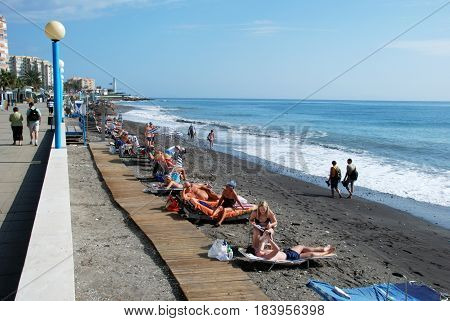 TORROX COSTA, SPAIN - OCTOBER 27, 2008 - Tourists relaxing on the beach with the promenade to the left hand side Torrox Costa Malaga Province Andalusia Spain Western Europe, October 27, 2008.