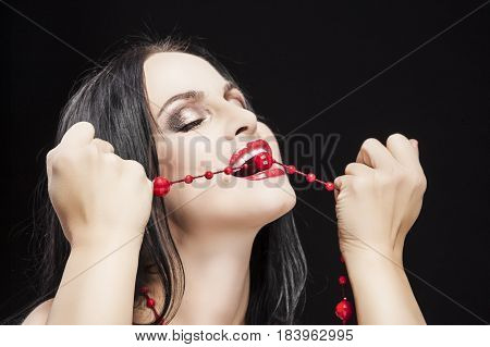 Sexual and Passionate Caucasian Brunette Woman Biting Her Long red Beads. Posing against Black.Horizontal Image