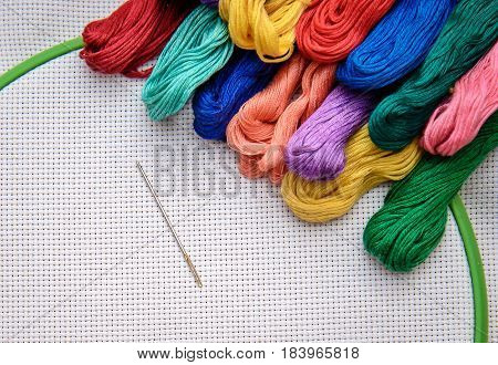 Bright embroidery floss in different colors nicely laid out on the canvas with the needle