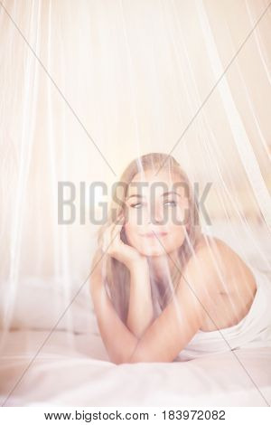 Dreamy woman lying down in the bed behind gentle net valance, fine art, creative photo, relaxation at home, peaceful holidays in spa resort