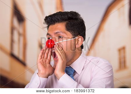 Funny handsome businessman with red plastic nose screaming.