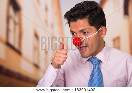 Funny handsome businessman with red plastic nose with his thumb up approving something