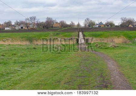 Pedestrian path through spring meadow to old foot-bridge over small river Tomakivka in Topyla village central Ukraine