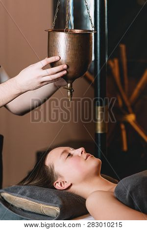 Specialist Making Shirodhara Massage Form Of Ayurveda Therapy. Beautiful Woman Spending Time At Mode