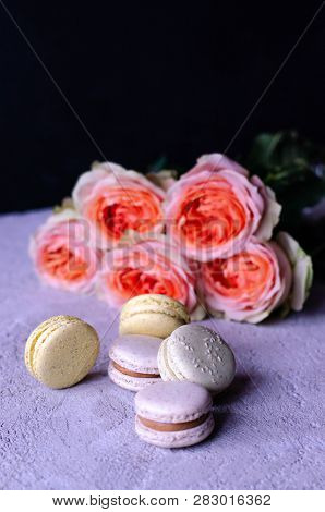 A Stack Of Macaroons With A Bouquet Of Beautiful Peach-colored Roses On A Gray Concrete Background.