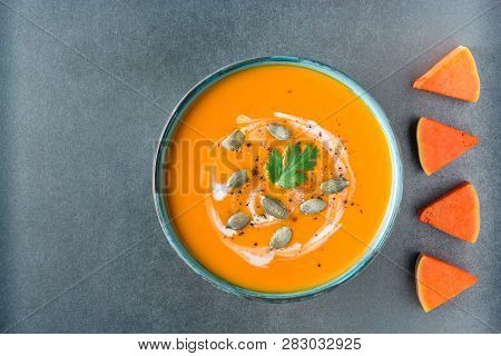 Bright Orange Pumpkin Soup In A Bowl, Pumpkin Slices And Seeds On Grey Background. Healthy Vegan Foo