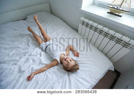 Happy Boy Playing In White Bedroom. Little Boy Brother Play On The Bed Wearing Pajamas. Family At Ho