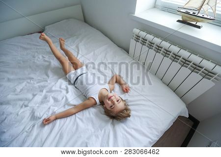 Happy Boy Playing In White Bedroom. Little Boy Brother Play On The Bed Wearing Pajamas. Family At Ho