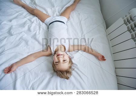 Happy Boy Playing In White Bedroom. Little Boy Brother Play On The Bed Wearing Pajamas. Family At Ho
