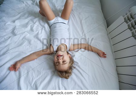 Happy Boy Playing In White Bedroom. Little Boy Brother Play On The Bed Wearing Pajamas. Family At Ho