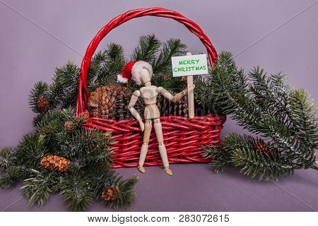 Merry Christmas Greetings Sign Held By Wooden Jointed Doll Standing Infront Of Large Red Backet Fill