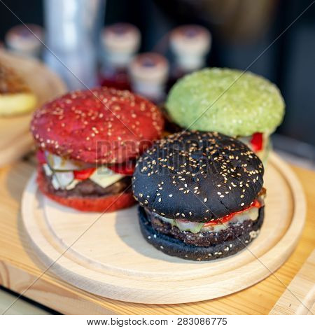 Three Tasty Bright Multicolored Beef Burgers On Wooden Counter At Food Fest. Amburger Bun Clolred Wi