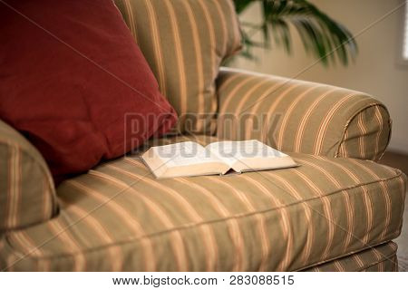 Open Book Resting On Warm, Inviting, Overstuffed Chair, Waiting To Be Read