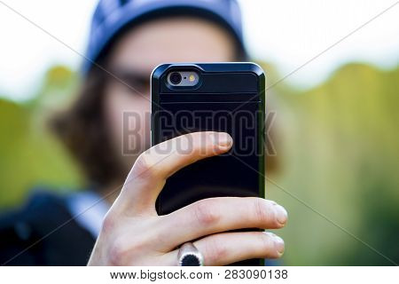 Unrecognizable Man With Long Hair, Wearing Warm Clothes And A Cap, Taking A Selfie Photo With His Sm