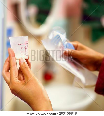 The Nurse's Hands Holding And Looking At Mother's Fresh Milk In A Medicine Measuring Glass Cup For A