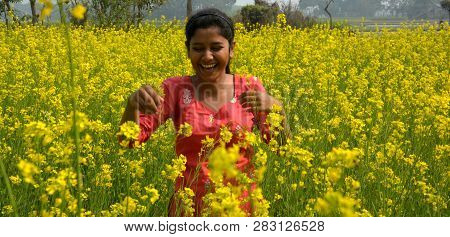 Close Up Of A Girl Wearing A Red Salwar  Laughing Heartly In A Sunny Day In A Rapeseed, Mustard Flow