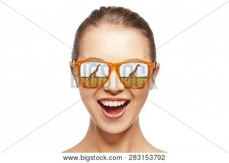 ecotourism and african safari concept - portrait of happy teenage girl in sunglasses looking at giraffes