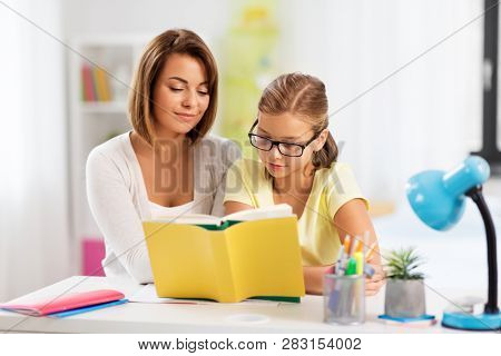 education, family and learning concept - mother and daughter doing homework together and reading book at home