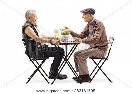 Full length profile shot of a mature punker drinking beer at a table and talking with an elderly man drinking coffee isolated on white background