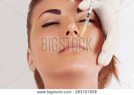 Portrait Of Beautiful Woman Gets Injection Of Botox In Her Lips. Closeup Hand In Glove With Syringe 