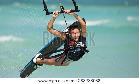 A Smiling Girl Performing A Relay Jump On A Kiteboard. The Subject Is Surrounded With Drops Of Water