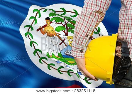 Belizean Engineer Is Holding Yellow Safety Helmet With Waving Belize Flag Background. Construction A