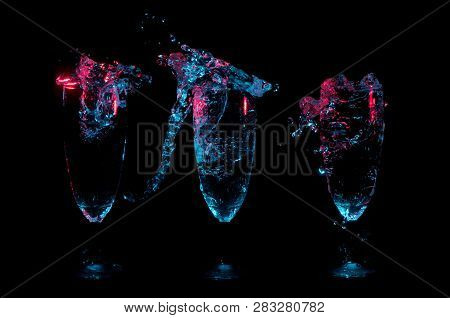Three Fancy Glasses In A Row Each With A Different Big Splash Of Liquid Under Blue And Red Lights On