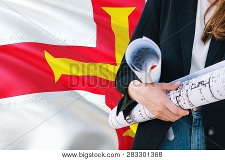 Architect Woman Holding Blueprint Against Guernsey Waving Flag Background. Construction And Architec
