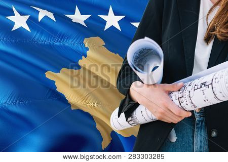 Architect Woman Holding Blueprint Against Kosovo Waving Flag Background. Construction And Architectu