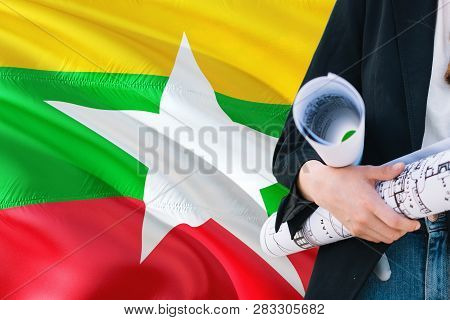 Burmese Architect Woman Holding Blueprint Against Burma Waving Flag Background. Construction And Arc