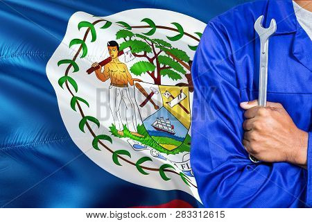 Belizean Mechanic In Blue Uniform Is Holding Wrench Against Waving Belize Flag Background. Crossed A