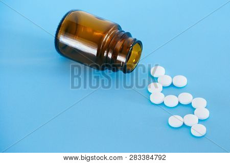 White Pills Spilling From A Medicine Bottle Forming A Dollar Sign On A Blue Background.