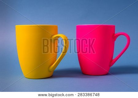 Big Yellow And Pink Mugs Isolated On Blue Background, Horizontal Orientation.