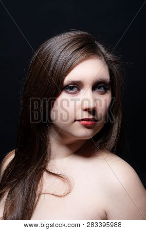 Beautiful gray-eyed brown-haired woman with red lips and bared shoulders against black background. C