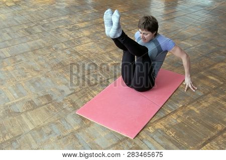 Sports Girl In Bodyflex Training. The Instructor In A Gray T-shirt On A Pink Rug Raises Her Legs To 