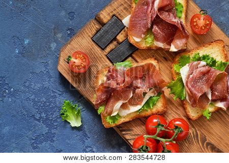 Bruschetta With Prosciutto, Salad Frieze And Cheese On The Kitchen Table. Snack. View From Above.