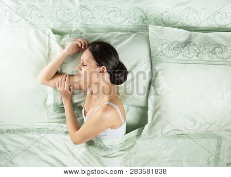 Beautiful young woman sleeping in luxury bed. Bed is made with linen embroidered percale. Space for text.