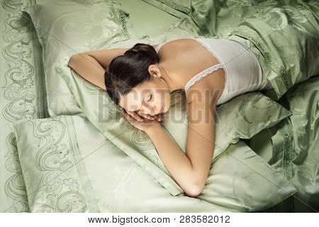Beautiful young woman sleeping in luxury bed. Bed is made with linen embroidered percale.