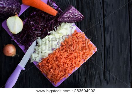 Chopped Fresh Blue Cabbage,onion And Carrot On The Violet Cutting Board On The Black Wooden Backgrou