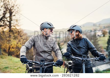 Active Senior Couple With Electrobikes Standing Outdoors On A Road In Nature.