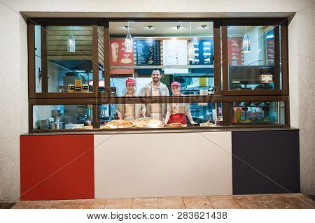 Smiling Young Stuff Aprons Selling Pizza In Fast Food Restaurant. Tasty Italian Food