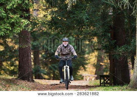 A Senior Man With Electrobike Cycling Outdoors On A Road In Park In Autumn.