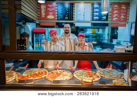 Smiling Young Stuff Aprons Selling Pizza In Fast Food Restaurant. Tasty Italian Food