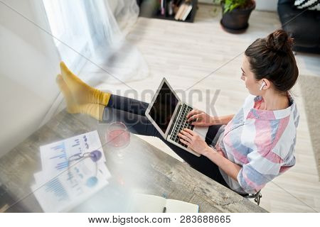 Above view portrait of relaxed young woman using laptop with feet on desk, copy space