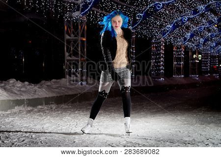 Girl With Blut Hair Skating On The Ice Arena In The Evening City Square In Winter