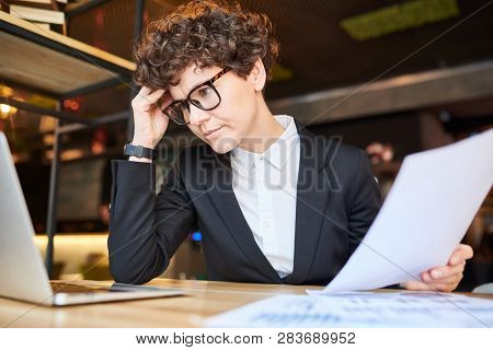 Pensive analyst touching her forehead while trying to concentrate on reading online information