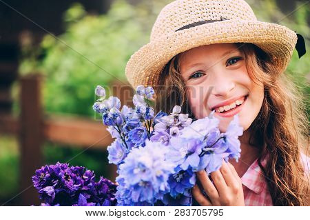 Romantic Portrait Of Happy Child Girl Picking Bouquet Of Beautiful Blue Delphinium Flowers From Summ